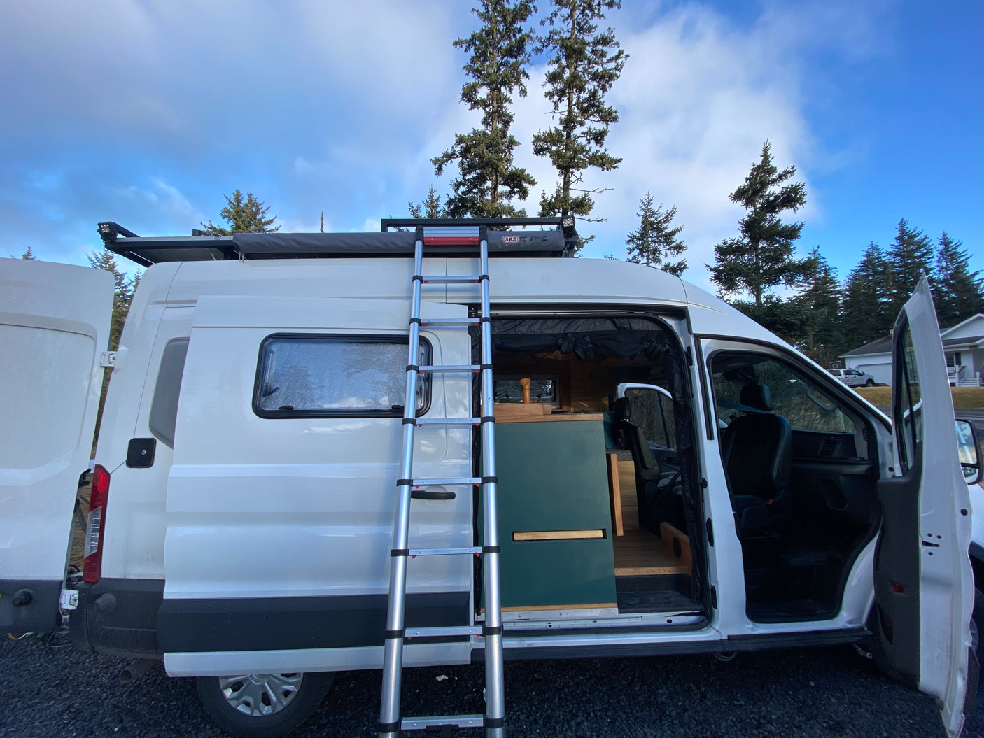 White RV rental camper van with open side door revealing a custom interior, ladder to roof, and awning.
