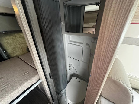 Explore this RV rental's compact interior: a functional bathroom with toilet, mirror, and shower, plus a cozy bunk bed.
