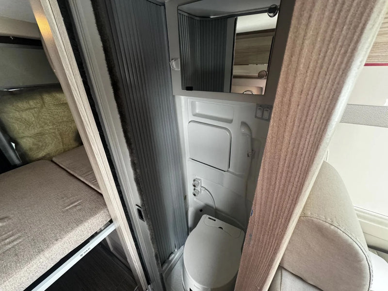 Explore this RV rental's compact interior: a functional bathroom with toilet, mirror, and shower, plus a cozy bunk bed. — photo 8