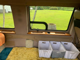 Cozy RV rental interior showing plush floor, green window view, and practical storage bins.