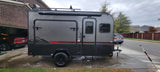 This grey Flyer teardrop RV rental, a compact off-road camper, is freshly washed and parked on a wet driveway.