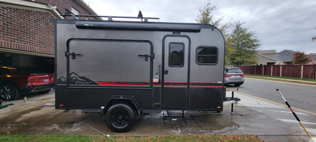This grey Flyer teardrop RV rental, a compact off-road camper, is freshly washed and parked on a wet driveway.
