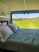 RV rental: interior bed with floral pillows, offering a window view of a vast, bright green field.