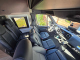 Spacious RV rental interior featuring multiple rows of black leather seating and a modern dashboard. Ideal for travel.