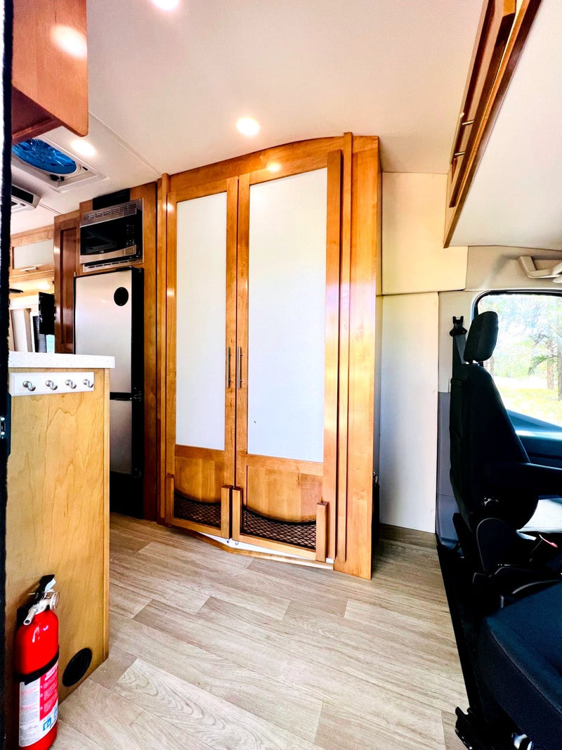Clean RV rental interior featuring warm wood cabinets with frosted glass, microwave, fridge, and light wood-look flooring. — photo 16