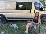 Happy woman & dog enjoying an outdoor camp with their RV rental. Relaxing by a camper van on grass.