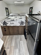 Cozy RV rental interior featuring a comfortable bed, compact kitchen with a mini-fridge, and light wood flooring.