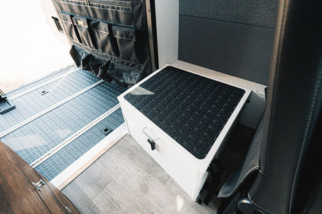 Inside an RV rental: versatile modular floor, door organizer, and a white storage/step box with textured top.