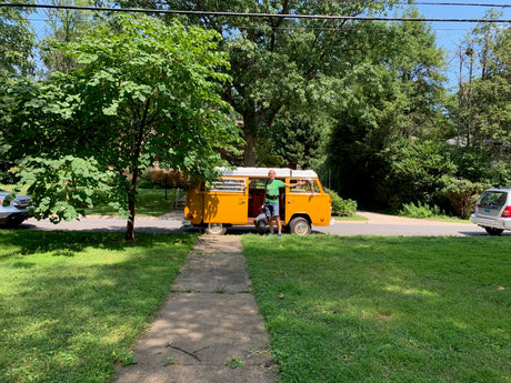 A man stands by a classic orange VW bus on a sunny street, an ideal RV rental ready for a scenic road trip adventure.