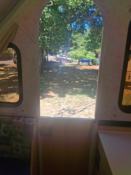 Inside an RV rental, a sunny view from the open door shows a grassy yard, trees, an SUV, and a child's toy car.