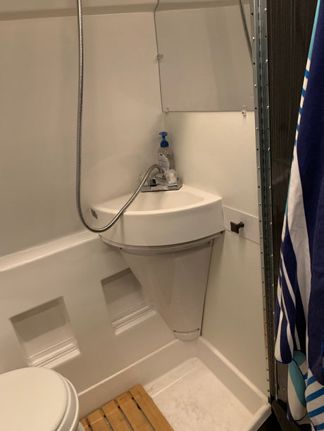 Inside an RV rental: a practical bathroom with a corner sink, a flexible shower hose, and a toilet.