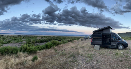 RV rental campervan set up for remote camping. A pop-top van sits on a gravel lot overlooking a vast, cloudy landscape at dusk.
