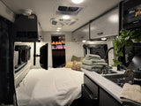 Cozy RV rental interior with a comfy bed, modern kitchenette, overhead controls, and beautiful sunset views. Ideal for road trips!