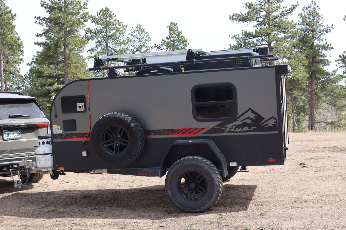 An inTech Flyer off-road camper trailer, a perfect RV rental option, hitched to an SUV in a natural setting.