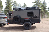 An inTech Flyer off-road camper trailer, a perfect RV rental option, hitched to an SUV in a natural setting.