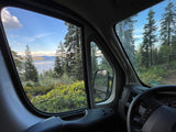 Inside an RV rental: a serene lake view with surrounding forest, seen from the driver's window.