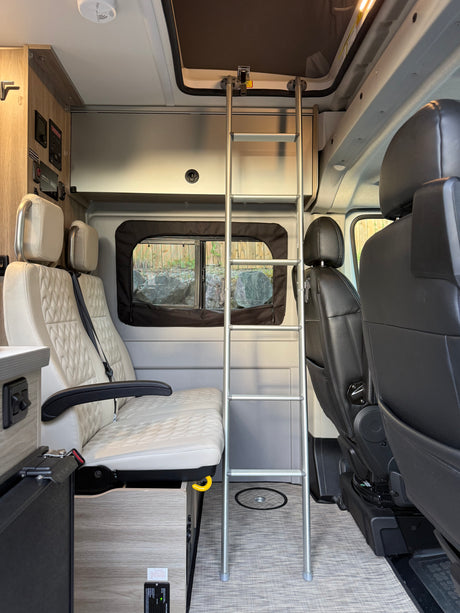 Modern RV rental interior with cream passenger seats, a bunk ladder, control panel, and textured flooring visible.
