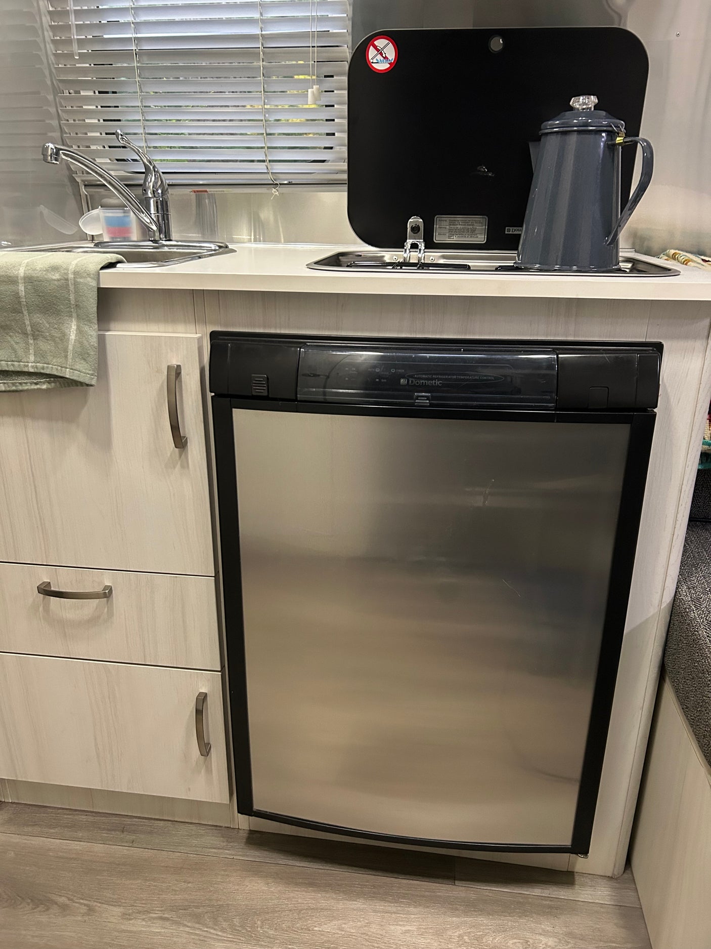 RV rental kitchen showing a Dometic refrigerator, sink, covered stovetop with coffee pot, and light-toned cabinets.