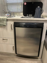 RV rental kitchen showing a Dometic refrigerator, sink, covered stovetop with coffee pot, and light-toned cabinets.