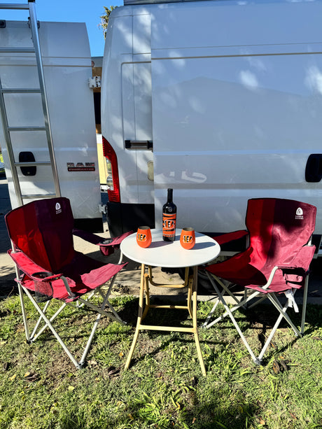 RV rental outdoor setup: White Ram ProMaster van with ladder, red chairs, table, & Bengals wine. Perfect for a stop.