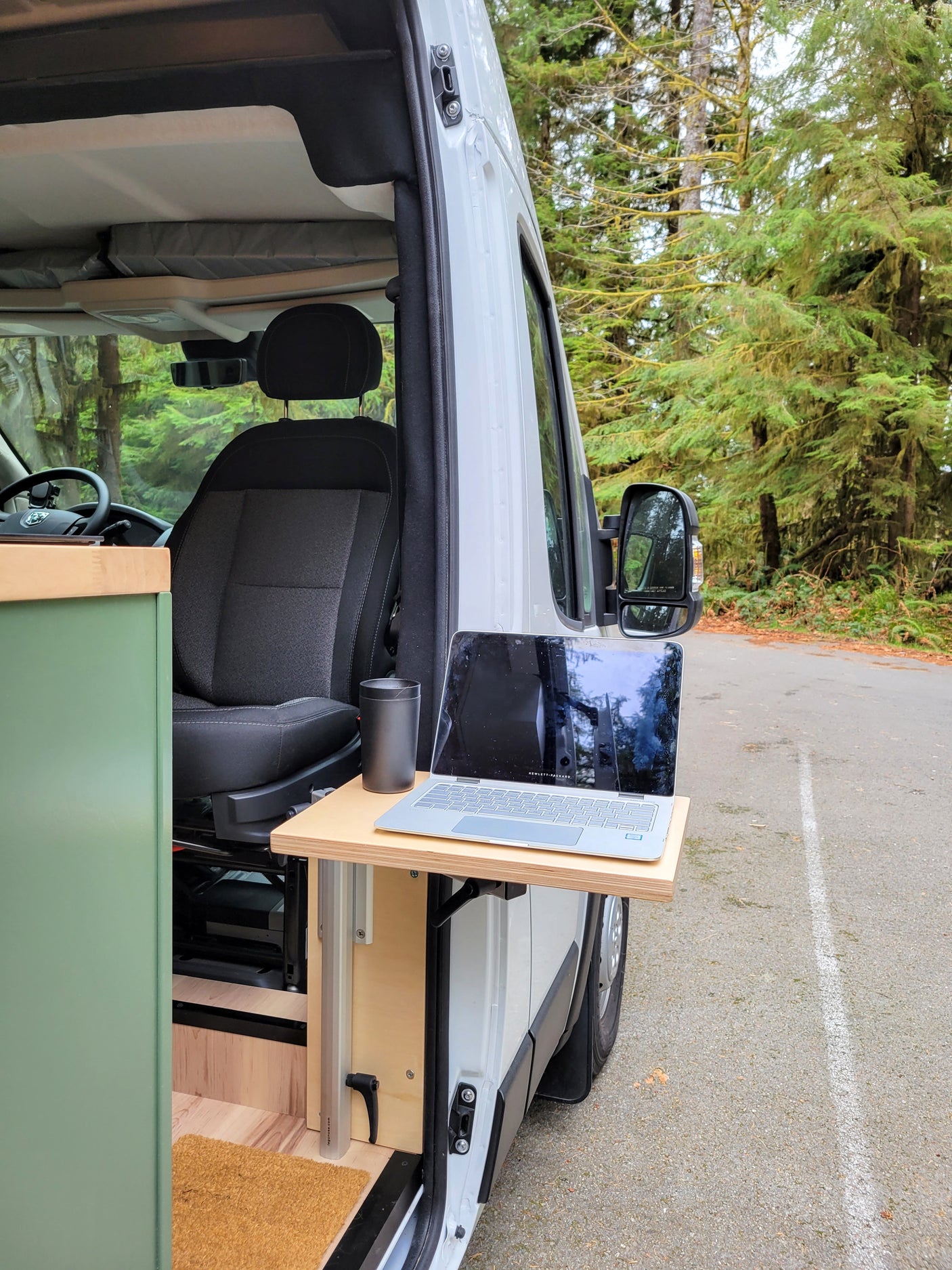 RV rental: A modern camper van with an exterior desk, laptop, and mug, perfect for remote work amidst nature.