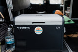 Inside an RV rental, a Dometic CFX portable cooler with an 'Outshine Adventures' sticker sits ready for your next adventure.