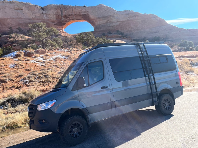  parked in a rocky mountain landscape.|Nighttime rv rental van adventure: A dark Mercedes Sprinter camper van under a bright moon and bare trees. Ideal for off-grid travel.|RV rental adventure: Grey camper van parked at a majestic natural arch in a snowy desert landscape under a clear sky.|Experience adventure with this RV rental! Interior view of a custom camper van featuring swivel seats — photo 3