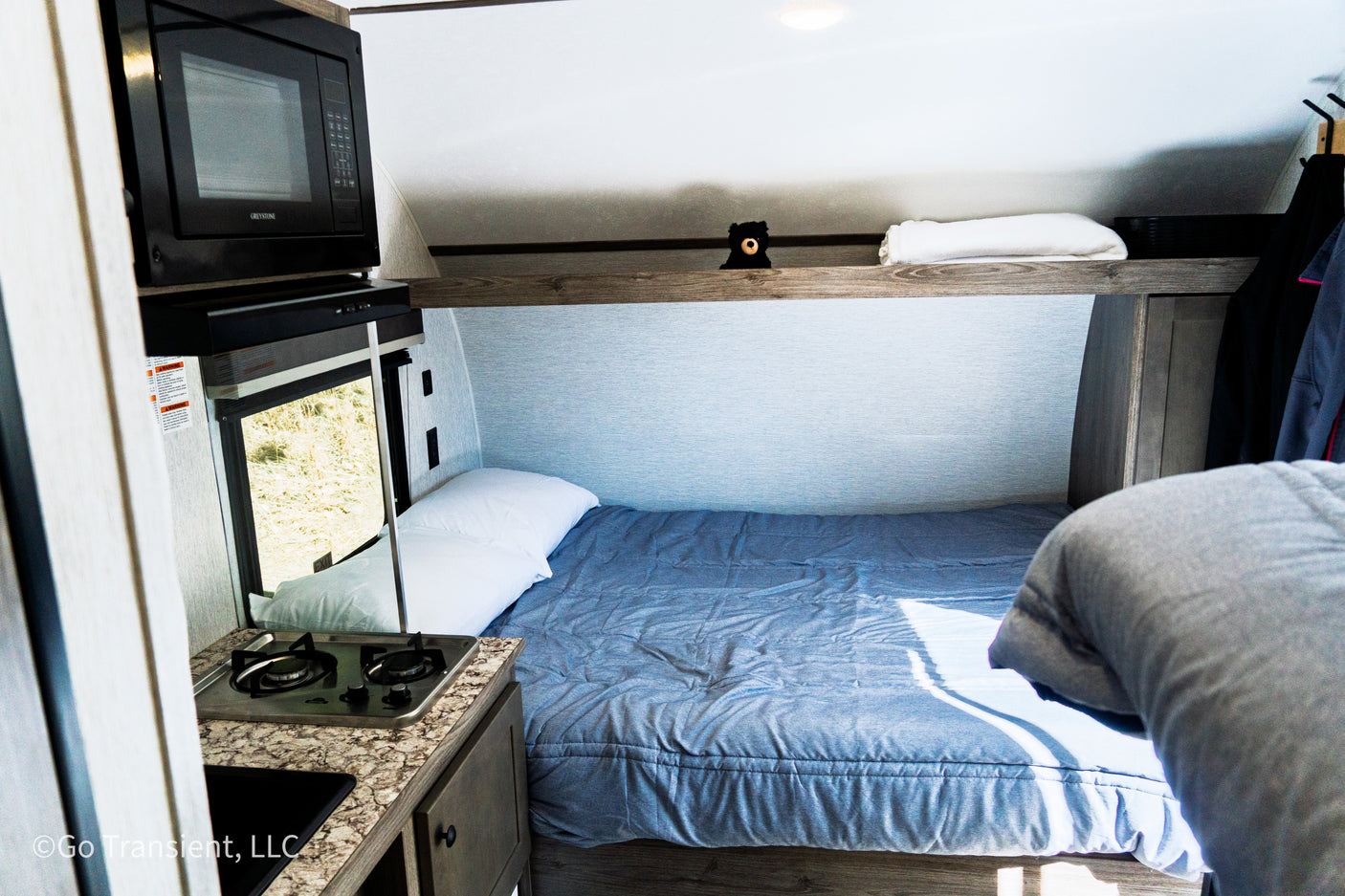 Inside this RV rental: a compact living area with bed, microwave, and stove for your travel comfort.