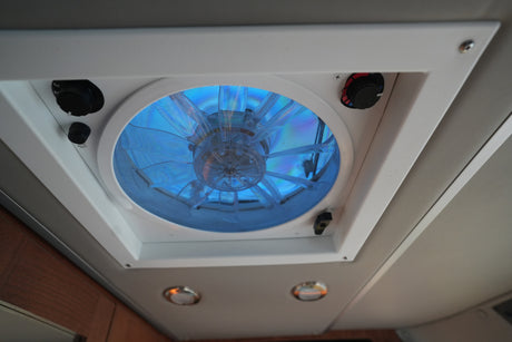 This RV rental ceiling vent fan features a glowing blue light, speed, and directional controls for ideal interior air circulation.