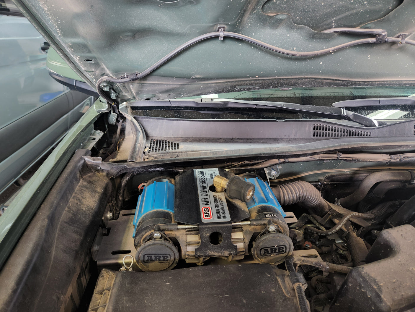 A dusty vehicle engine bay reveals an ARB air compressor. A practical addition for maintaining tires during an RV rental adventure.