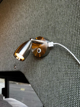 Close-up of a brushed metal reading light and USB port, mounted on a green woven fabric wall, ideal for an RV rental. Light glows warmly.