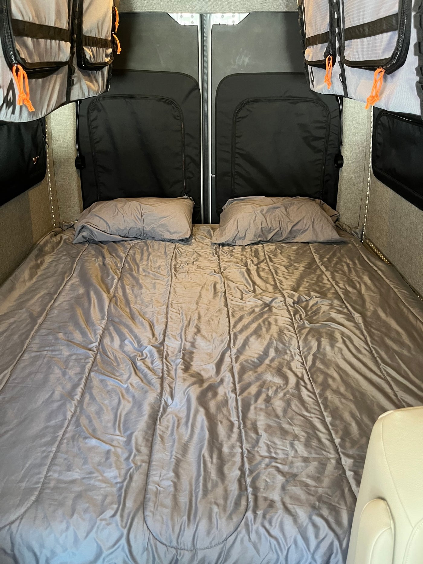 Spacious RV rental interior featuring a comfy bed with pillows, storage bags, and practical lighting. — photo 8