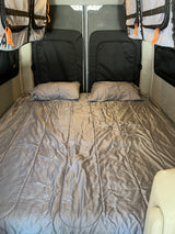 Spacious RV rental interior featuring a comfy bed with pillows, storage bags, and practical lighting.