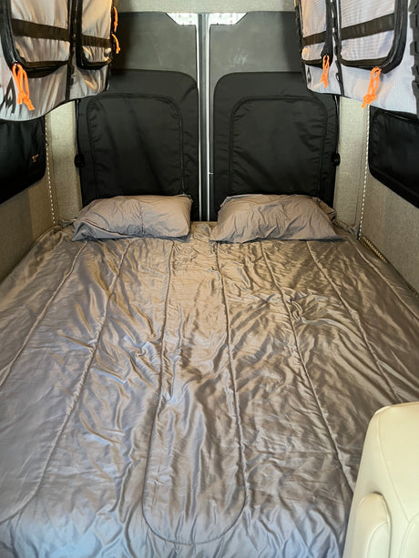 Spacious RV rental interior featuring a comfy bed with pillows, storage bags, and practical lighting.