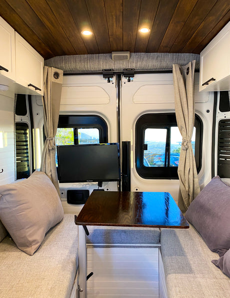 This cozy RV rental interior features a wood ceiling, TV, table, and comfy bench seating for travel comfort.