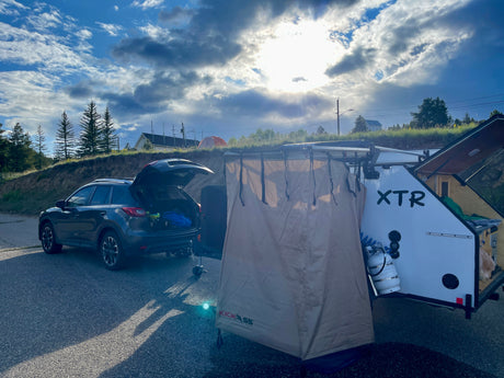 SUV & XTR teardrop trailer RV rental setup with an outdoor shower tent, ready for camping under a bright sky.