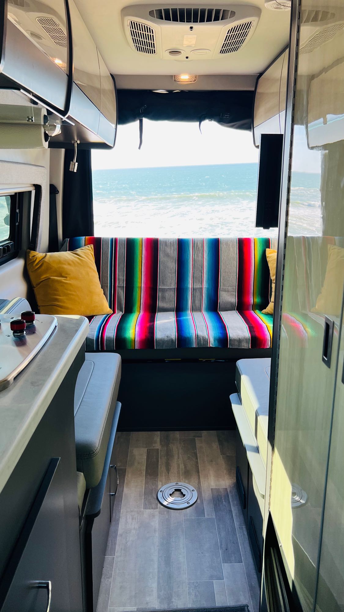 Enjoy the stunning ocean view from this cozy RV rental's interior, featuring a colorful bench and kitchen area.
