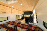 Bright and modern rv rental interior featuring custom wood ceilings, overhead cabinets, a cozy bed, and a full kitchen.