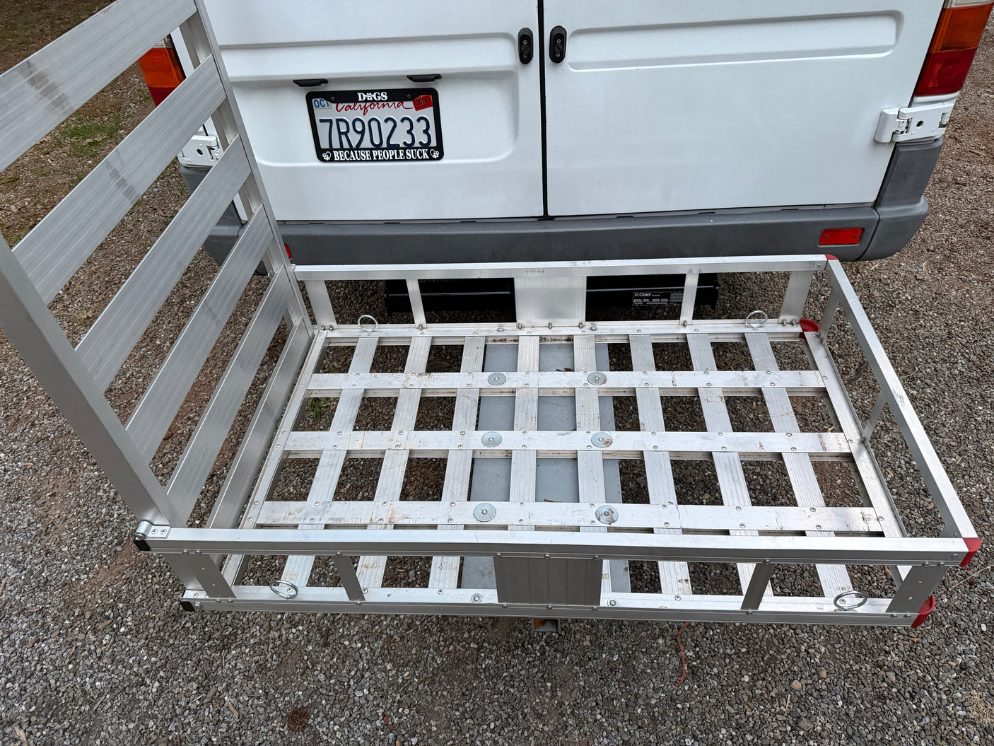 Hitch-mounted aluminum cargo carrier on RV rental van with ramp in upright position.
