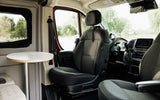 Experience comfort in our RV rental! Swiveled driver's seat and table in a cozy camper van interior.