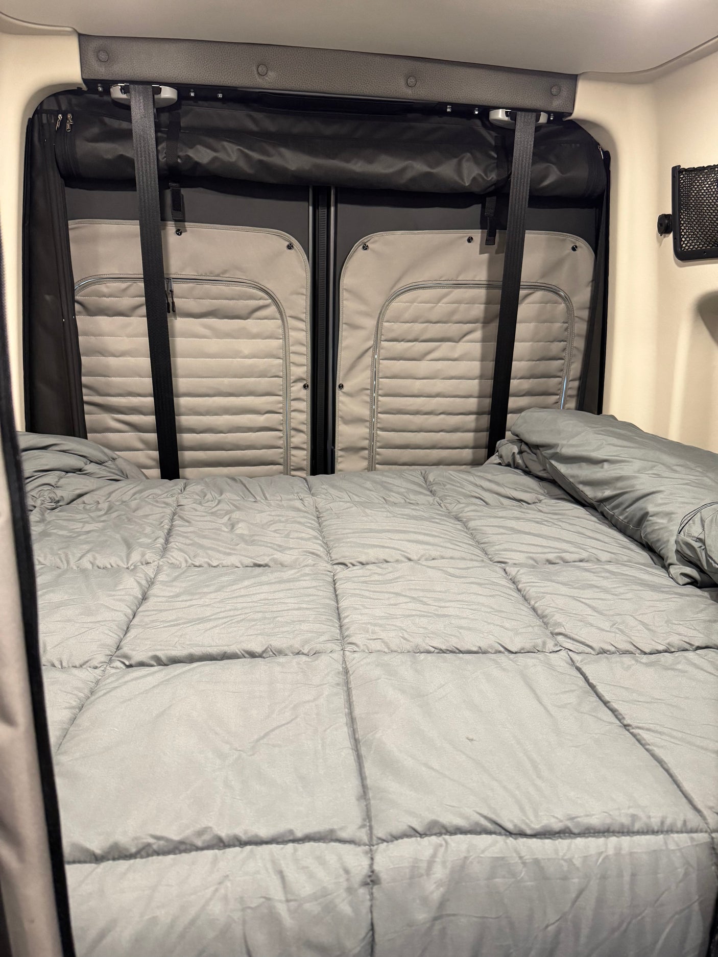 Comfortable sleeping area in an rv rental, featuring a bed with a grey comforter and padded rear door panels.