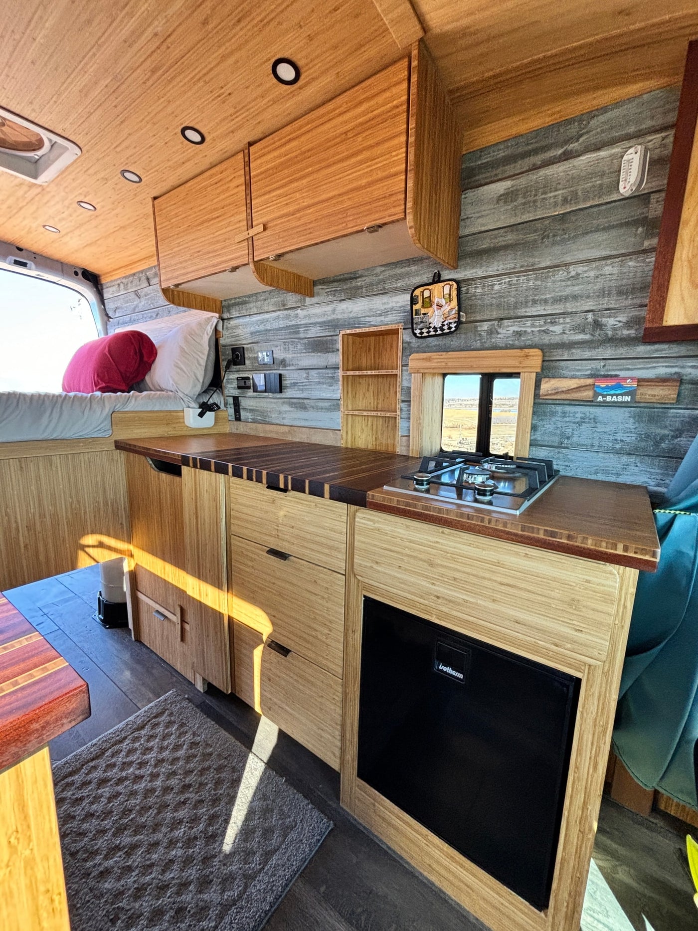 Inside an RV rental: a modern bamboo interior with kitchen, stove, fridge, and cozy bed. Wood paneling & natural light. — photo 10