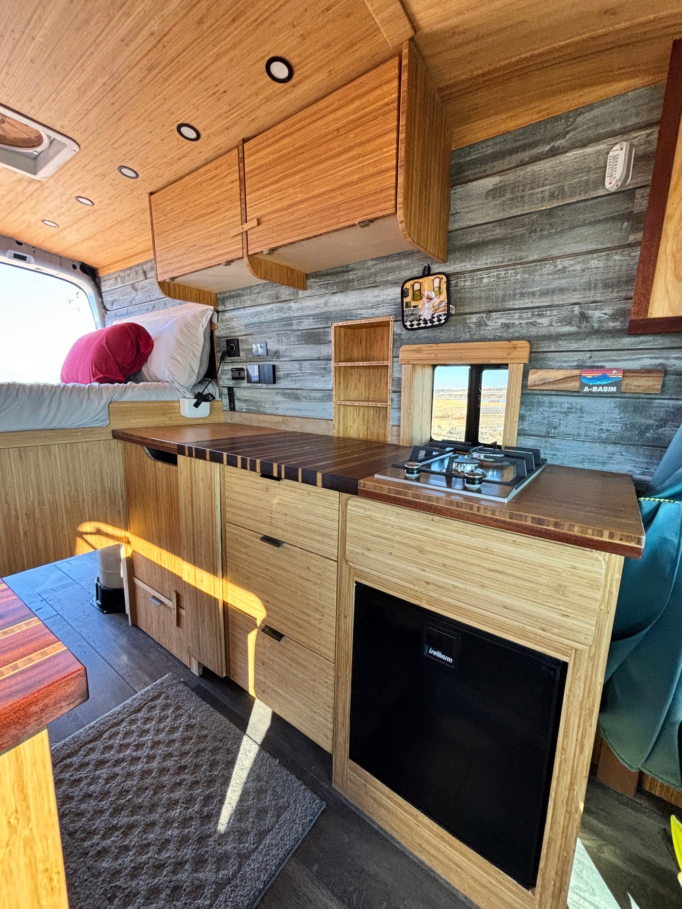 Inside an RV rental: a modern bamboo interior with kitchen, stove, fridge, and cozy bed. Wood paneling & natural light.