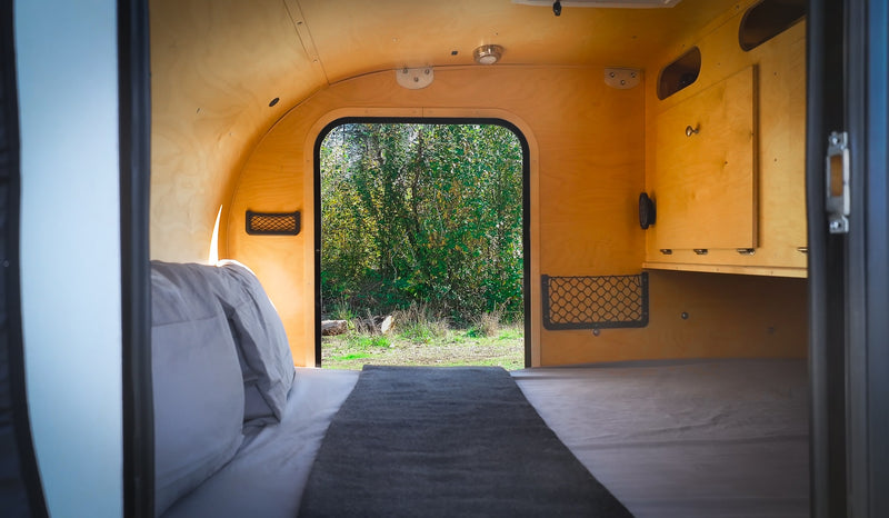 Inside a cozy RV rental: comfy bed, wooden interior, and serene forest views. Ideal for your next travel adventure. — photo 5