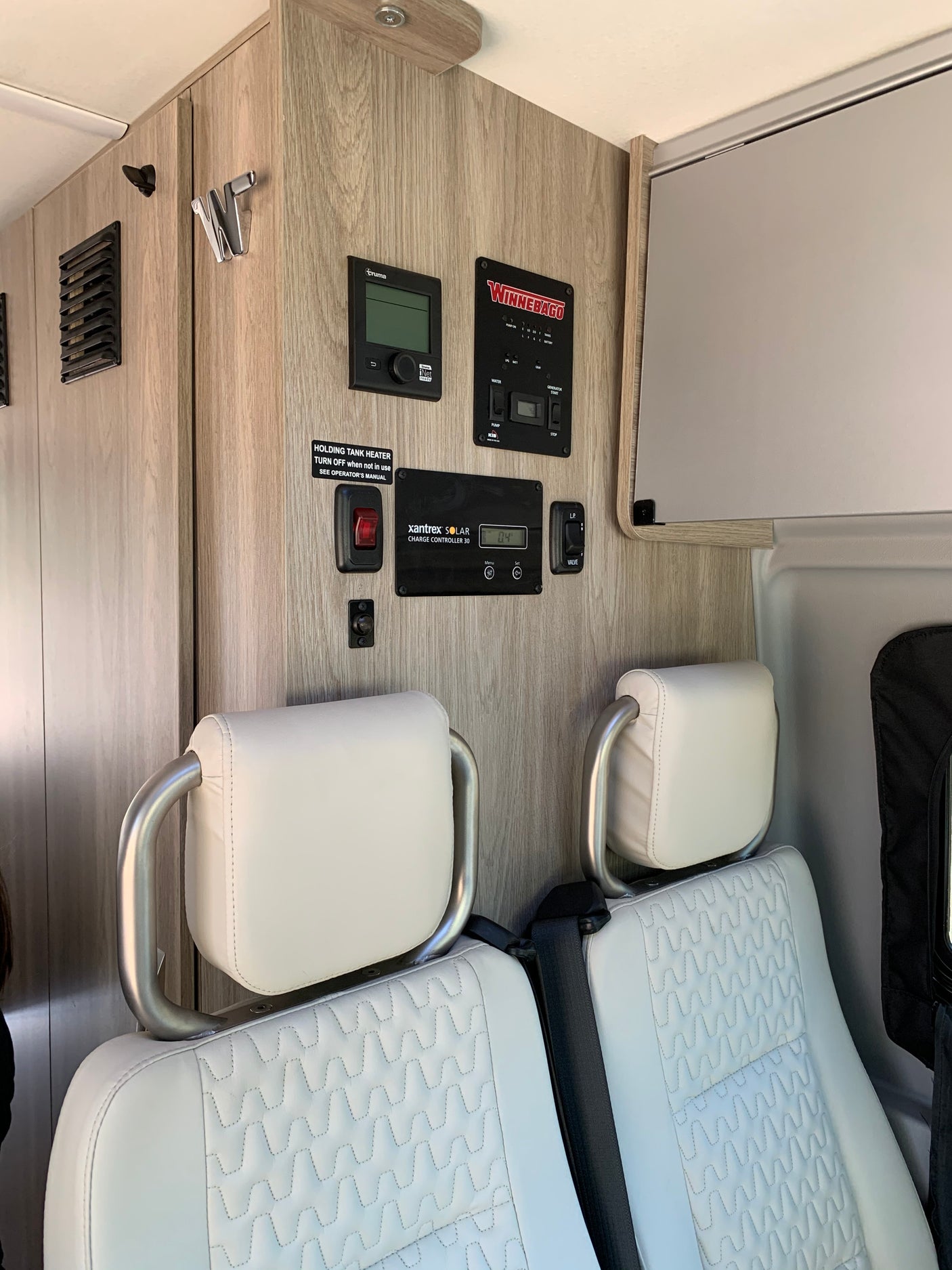 RV rental interior showing control panels for solar, water, and power systems, plus comfortable white seating.