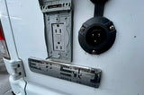 RV rental: Exterior of a white utility van featuring a weatherproof GFCI outlet and a black shore power inlet for outdoor electrical access.