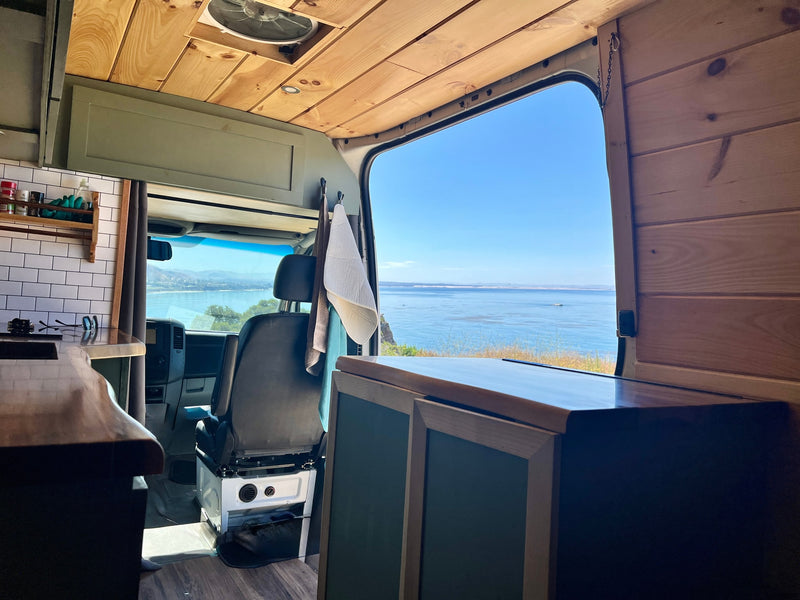 Immerse in van life with this RV rental! Interior shows wooden ceiling, kitchen, and a stunning ocean view from the open door. — photo 11