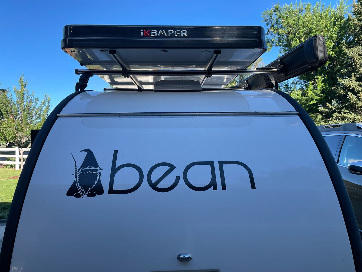 White teardrop camper RV rental with iKamper roof tent, side awning, and custom "ABean" gnome logo.