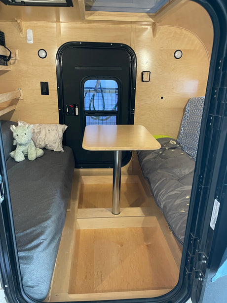 Cozy rv rental: small camper interior with two narrow beds, a central table, and light wooden walls. A stuffed animal sits on the left bed.