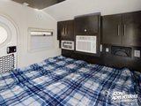 Cozy rv rental bedroom interior with a plaid bed, overhead cabinets, window, and AC units for comfortable travel.